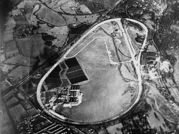 Aerial photograph of the Brooklands circuit: a banked oval track enclosing the airfield, with sheds and factory buildings along one side